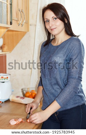 Young woman cutting a sausage on a cutting board in kitchen