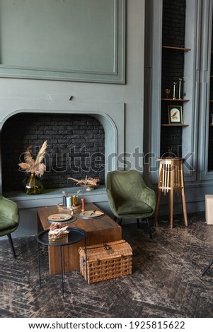 A beautiful luxurious interior of the room with an armchair against a dark blue wall. dark wooden floor. Green armchair near table Royalty-Free Stock Photo #1925815622