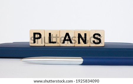 The text Plans on a wooden cubes, lying on a Notepad with a metal blue pen. Business concept photo