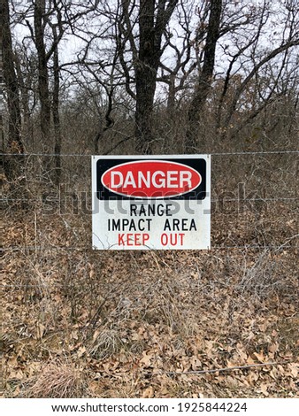 A warning sign attached to a chain link fence that reads Danger Range Impact Area near a military base training facility