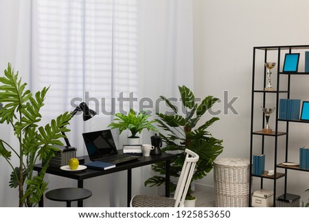 In the house, in the living room, there is a separate space for a workstation with a laptop when working remotely. The laptop is on the black table and right next to it is a coffee mug, a fresh green