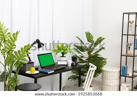 In the house, in the living room, there is a separate space for a workstation with a laptop when working remotely. The laptop is on the black table and right next to it is a coffee mug, a fresh green