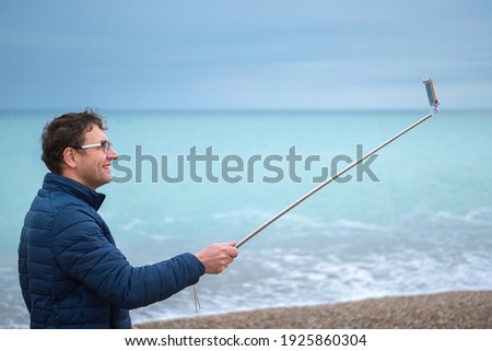 Young man on the beach with a smartphone on a selfie stick.