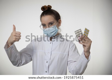 Doctor therapist woman in medical mask shows thumb up approving recommending pills, tablets medicines. Female GP or physician advise medication dietary supplements or vitamins. Healthcare concept.