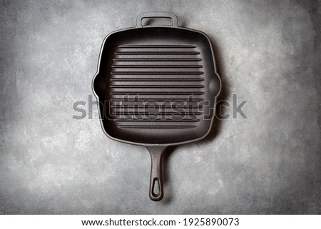 Black iron empty grill pan on gray concrette background. top view