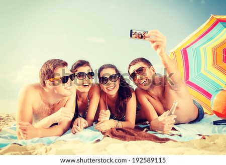 summer, holidays, vacation, technology and happiness concept - group of smiling people in sunglasses taking picture with smartphone on beach