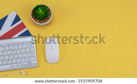 Mouse, keyboard with English flag and headphones on the left against a yellow background with space for text on the right, close-up top view.
