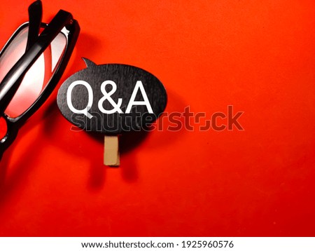 Selective focus.Word QNA on black board with glasses on red background.Shot were noise and film grain.