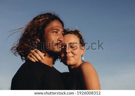 Against the blue sky, the face of a man with An Asian appearance and the snuggled face of a woman with eyes closed in appearance. High quality photo