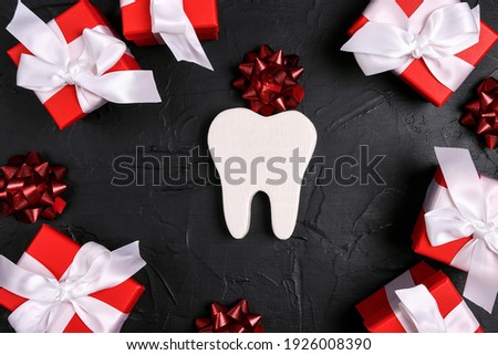 Festive dental background with tooth surrounded by red gifts and bows on a black background with copy space for text. Happy Dentist's Day concept .
