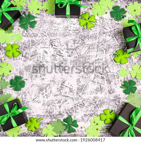 Saint Patrick's Day concept. Frame of decorative clover leaves and gift boxes on grey background. Top down flat lay composition with copy space.
