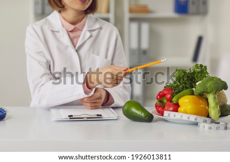 Telehealth and online nutritiologist concept. Woman doctor nutritiologist sitting and pointing at fresh vegan healthy ingredients to patient online during videocall or distant meeting Royalty-Free Stock Photo #1926013811
