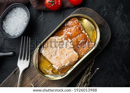 Salmon, fish preserves Canned smoked fish set, on wooden cutting board, on black background with herbs and ingredients, top view flat lay