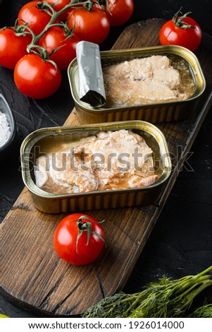 Canned salmon, fish preserves set, on wooden cutting board, on black background with herbs and ingredients