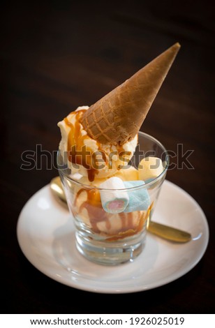 Vanilla ice cream cone in a cup and topped with caramel on a dark background.