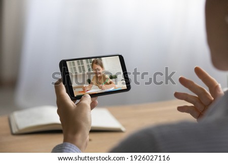 Back view of female teacher have webcam online lesson with small schoolgirl using smartphone. Woman or mom talk on video call study distant with little girl child on cellphone. Technology concept.