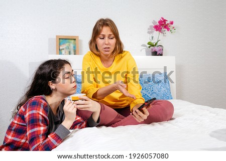Two young Caucasian women are relaxing in the bedroom, chatting and appraising something on their smartphone. Concept of LGBT relations and social networks.