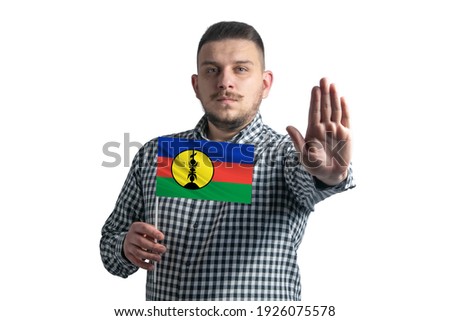 White guy holding a flag of New Caledonia and with a serious face shows a hand stop sign isolated on a white background.