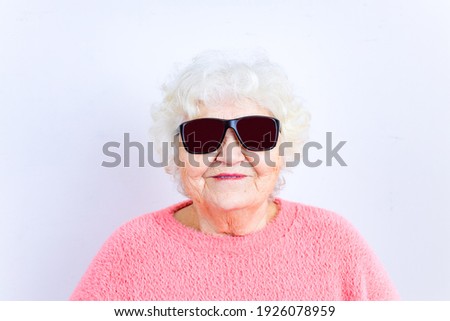 Portrait of funny senior blonde woman in sun glasses and pink sweater on white background