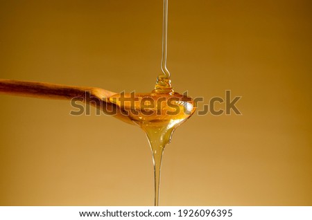 Spoon with a pouring drop of golden honey on yellow background. Royalty-Free Stock Photo #1926096395