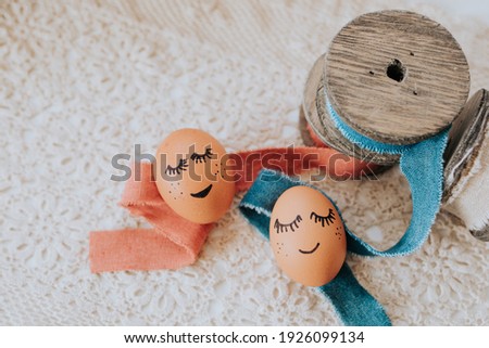 brown easter eggs with painted face lie on a crochet blanket and linen ribbons with wood are decorated to it
