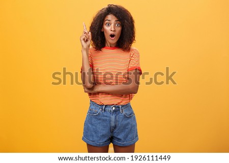 Girl finally understood riddle adding suggestion outloud. Excited thrilled good-looking dark-skinned woman staring amazed raising index finger in eureka gesture having idea over orange wall Royalty-Free Stock Photo #1926111449