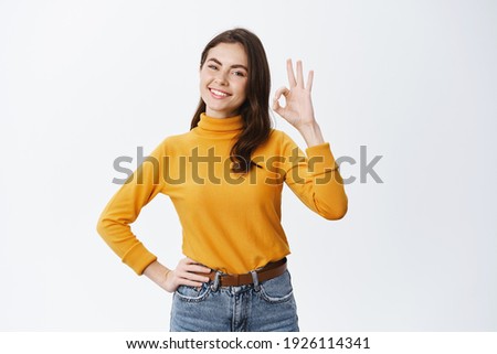 Alright. Smiling young woman hold all under control, show okay sign and looking confident, guarantee quality, advertising good product, standing against white background. Royalty-Free Stock Photo #1926114341
