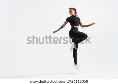 Woman in sportwear doing jump workout and look behind at empty space for logo. Female athlete with fit body exercising on white background, training with happy smile. Royalty-Free Stock Photo #1926118058