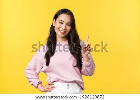 People emotions, lifestyle and fashion concept. Smiling happy good-looking asian girl giving advice, showing one finger as explain rules, make point, standing yellow background Royalty-Free Stock Photo #1926120872