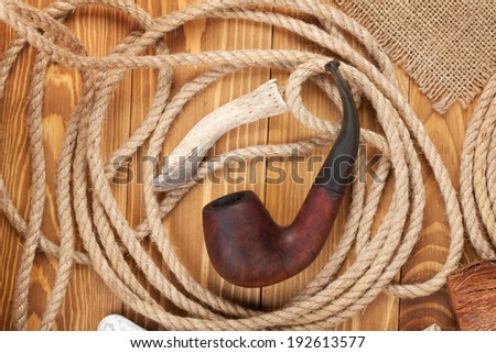 Tobacco pipe and rope on wooden background