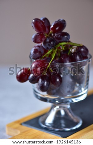 Dark purple grapes in a glass goblet on a slate and bamboo stand.
