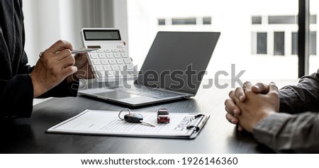 A car rental company employee holds a white calculator to show the tenant the rental price, the employee calculates the cost of the car rental before entering into the lease agreement with the renter. Royalty-Free Stock Photo #1926146360
