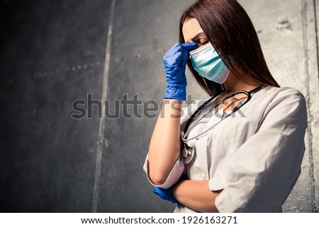 Nurse worker have headache migraine close eyes feel bad pain tired owerworked. Female doctor dressed medical white gown with stethoscope blue disposable face mask and gloves
