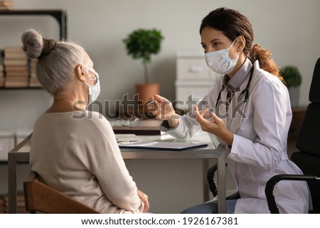 Close up serious doctor wearing medical face mask consulting mature woman patient at appointment in office, physician explaining treatment, giving recommendations, elderly generation healthcare Royalty-Free Stock Photo #1926167381