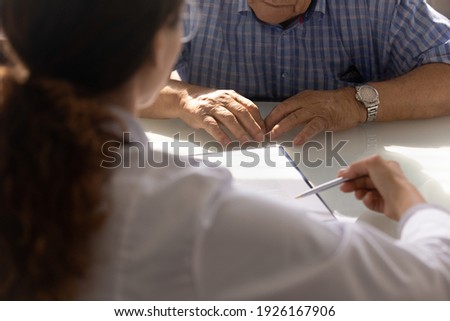 Close up female doctor consulting mature man about health insurance agreement, pointing pen at document, therapist physician and elderly patient discussing contract terms, healthcare concept
