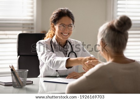 Close up smiling female doctor wearing glasses and uniform with stethoscope shaking mature woman hand at meeting, elderly patient making health insurance deal, older generation healthcare concept Royalty-Free Stock Photo #1926169703