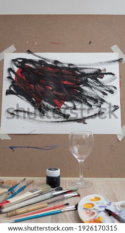Artist's workplace. Among the brushes and paints is a glass of red wine. Two hearts are depicted on the canvas as a symbol of love. Lack of inspiration, depression concept, alcoholism. Denial of love