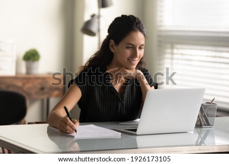Smiling woman looking at laptop screen, watching webinar or lecture, online course, taking notes, sitting at desk, motivated young female student studying, businesswoman freelancer working on project Royalty-Free Stock Photo #1926173105