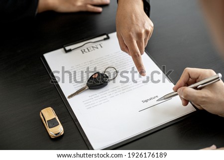An employee of the rental car company points to the contract document in the Renter's signature box to have the tenant sign the rental agreement to agree to the rental agreement. Concept car rental. Royalty-Free Stock Photo #1926176189
