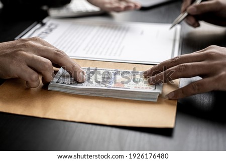 The company's procurement manager is contracting a partner company, accepting large amounts of bribes in dollar bills to cooperate in defrauding the company, fraud is illegal and immoral. Royalty-Free Stock Photo #1926176480