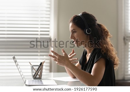Profile view close up woman in headphones chatting online, using laptop, teacher leading lesson, recording webinar, explaining, teaching students, distance education, businesswoman consulting client Royalty-Free Stock Photo #1926177590