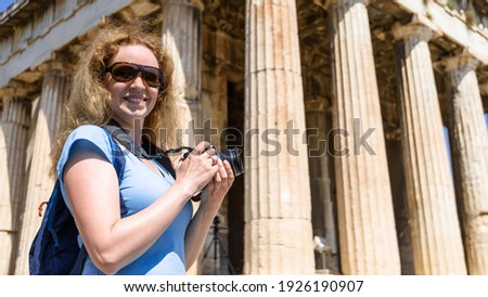 Tourist with camera visits Temple of Hephaestus, Athens, Greece. It is landmark of Athens. Young woman photographs ancient Greek building in Athens center. Concept of travel and sightseeing in Athens.