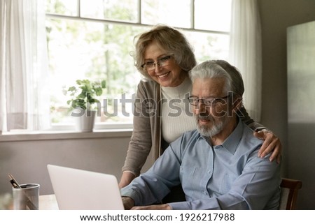 Happy mature OAP couple study internet app on laptop, grandparents use computer at home for online shopping. Smiling middle aged pensioner wife hugs senior husband during video call to relations Royalty-Free Stock Photo #1926217988