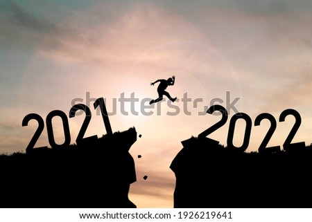 Welcome merry Christmas and happy new year in 2022,Silhouette Man jumping from 2021cliff to 2022 cliff with cloud sky and sunlight. Royalty-Free Stock Photo #1926219641