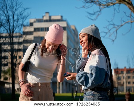 two young girls using a smartphone and earphones, looking happy and wearing casual clothes