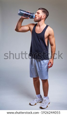 Young bearded handsome sporty man in sport clothing standing and drinking water on white background Royalty-Free Stock Photo #1926244055
