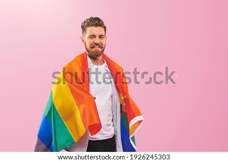 Portrait of smiling Handsome bearded young hipster gay covered in lgbtq+ flag on pink background