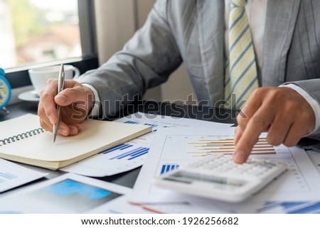 Asian male finance staff is calculating the investment results to deliver a report to his supervisor at the meeting. On the table in the office, the concept of calculating investment results 