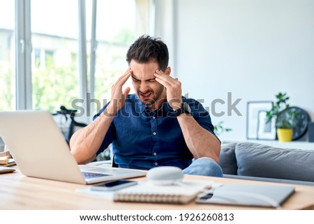 Young man suffering migraine pain while working at home Royalty-Free Stock Photo #1926260813