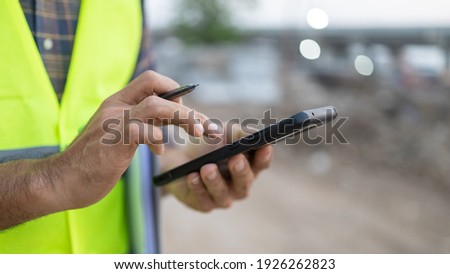Close up construction worker holding a pen using a smartphone construction site Royalty-Free Stock Photo #1926262823